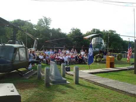 Veterans and families seated between two Vietnam era helicopters, the UH-1 Huey and the UH-34 Seahorse.