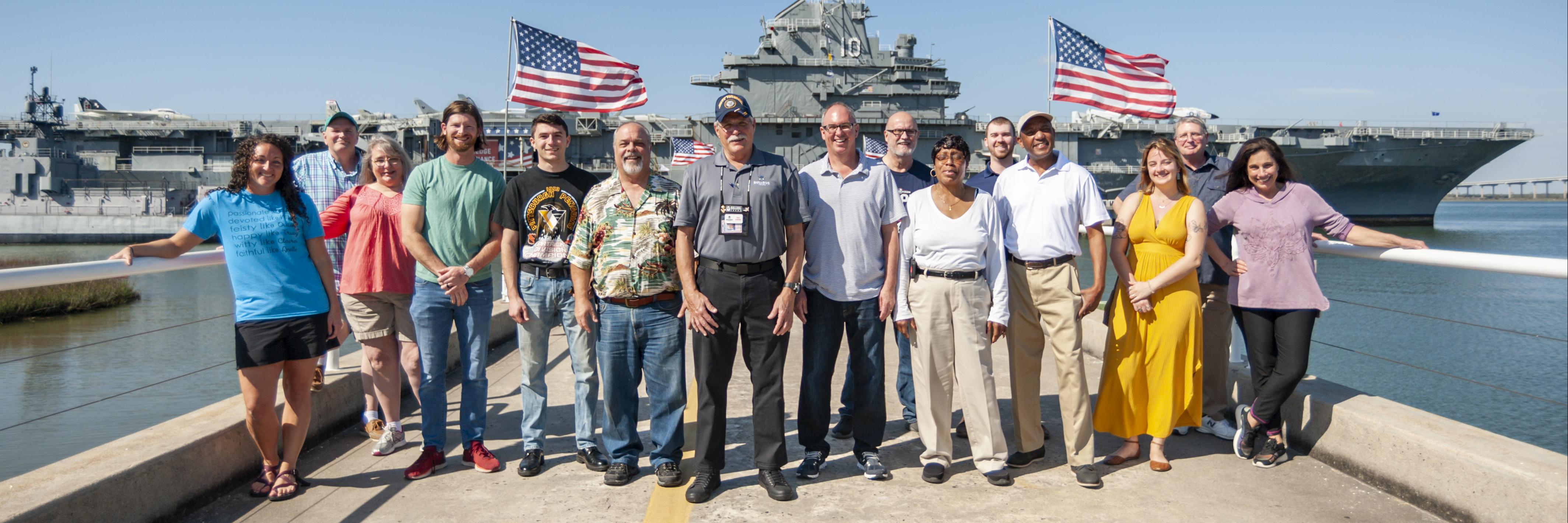 A group stands on the pier in front of the USS Yorktown.