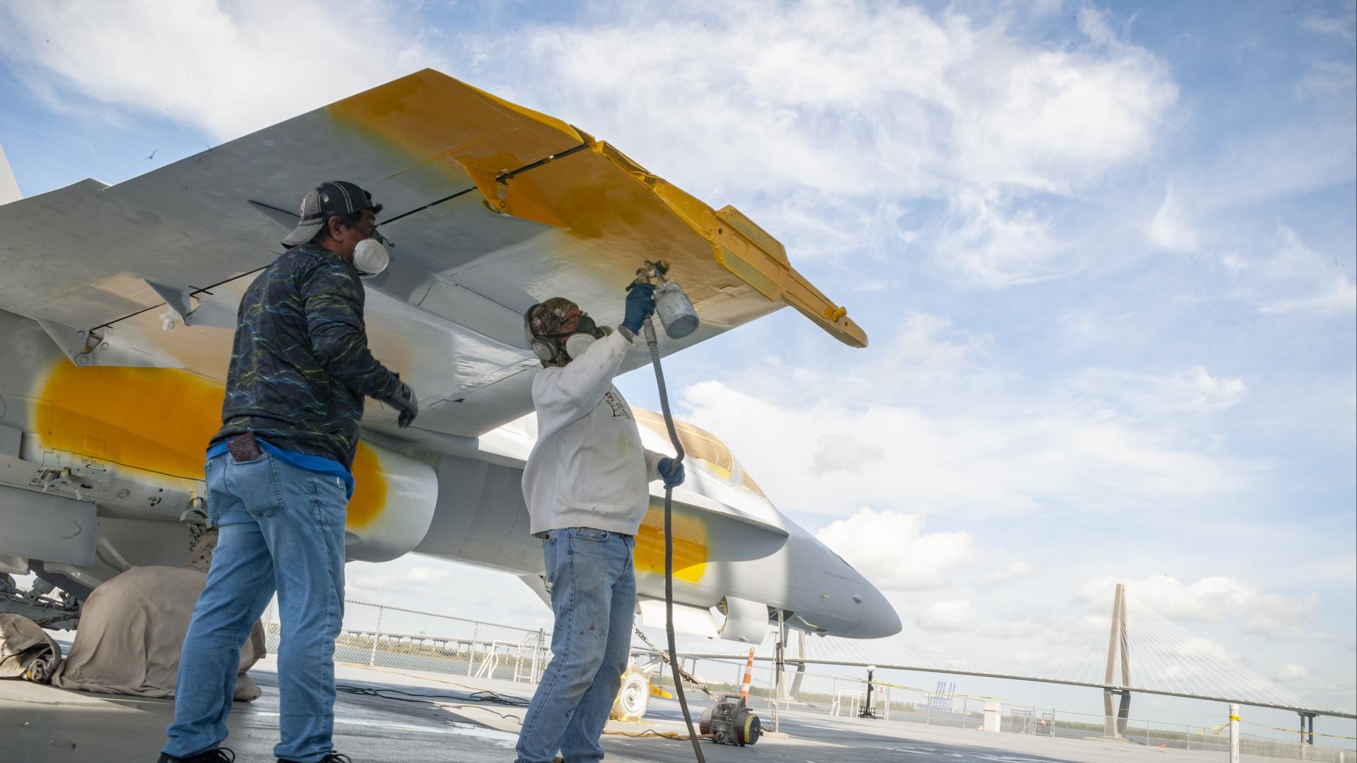 Two men repainting the wings of an aircraft