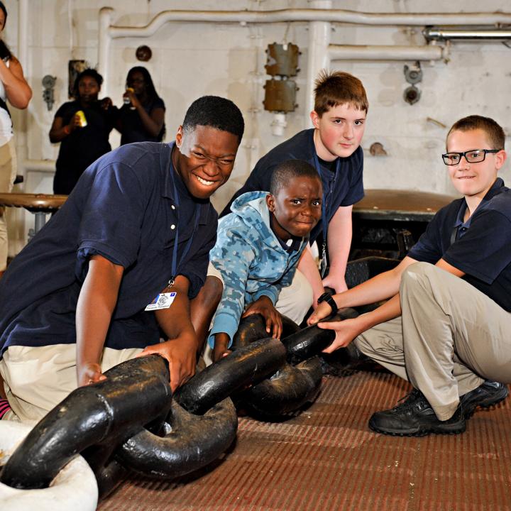Four boys trying to pull on an anchor chain