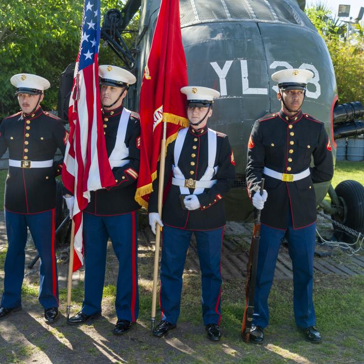 Honor guards salute in front of a Vietnam-era helicopter during a Vietnam Veterans Day event.