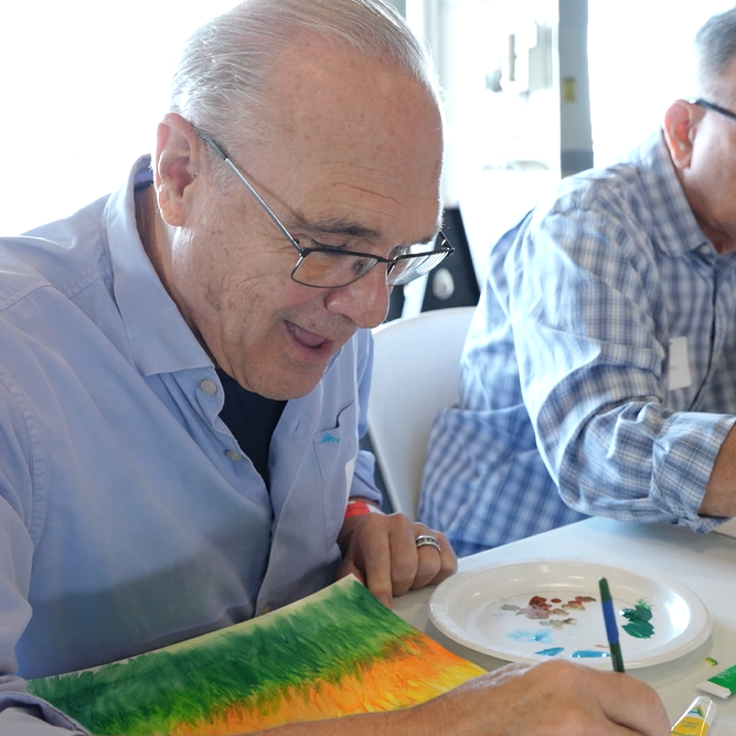 Two veterans sit while painting as they participate in the Patriot Art experience aboard the USS Yorktown (CV-10).