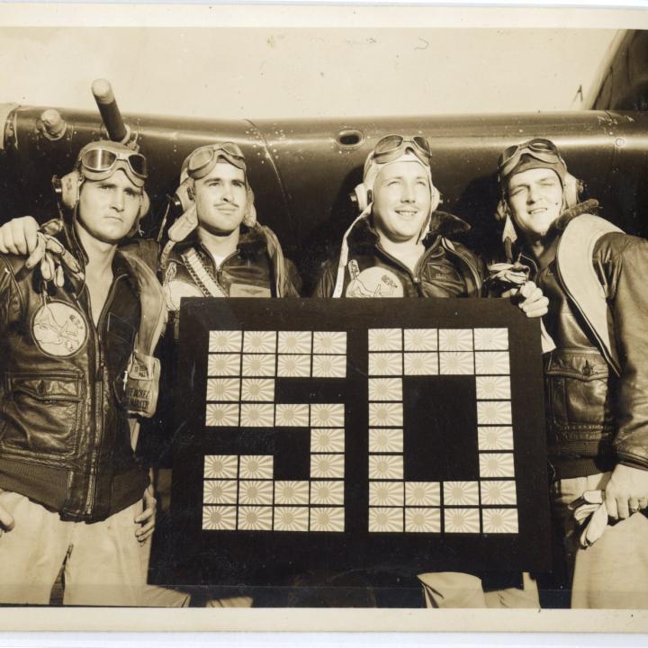 Vintage photo of four mean posing in front of an airplane.