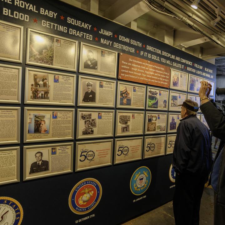 Visitors take photos of the wall featuring framed stories of volunteers' military service.