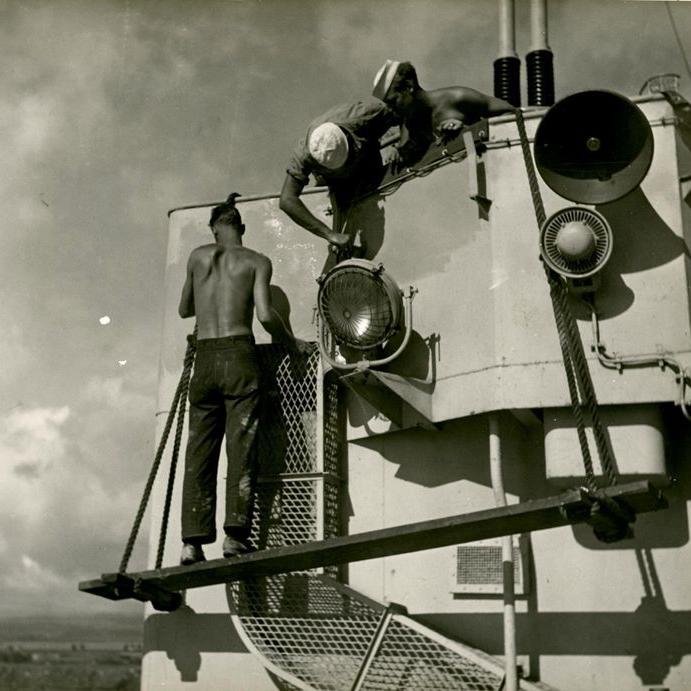 3 sailors standing outside doing work on one of Laffey's 40 mm gun mounts.