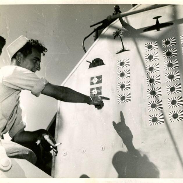 Signalman Theodore "Frank" Purrick pointing to the killboard on the USS Laffey.