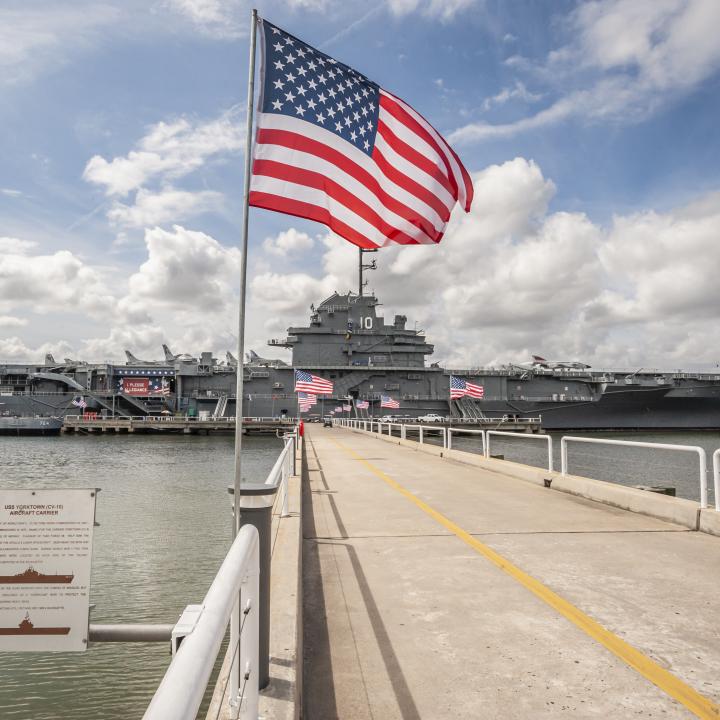 An American Flag waving in the foreground with the USS Yorktown behind.