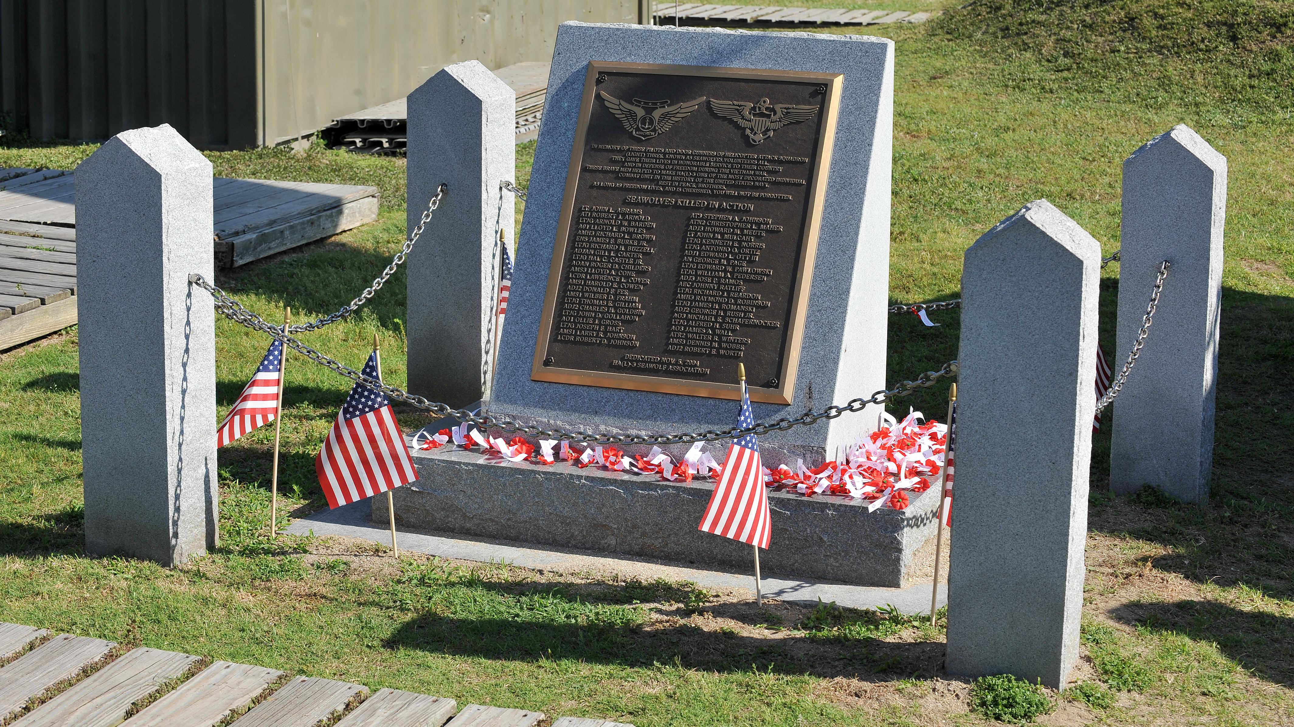 Memorial monument featuring a plaque engraved with the names of servicemembers killed in action, surrounded by small American flags and red, white, and blue decorations. 