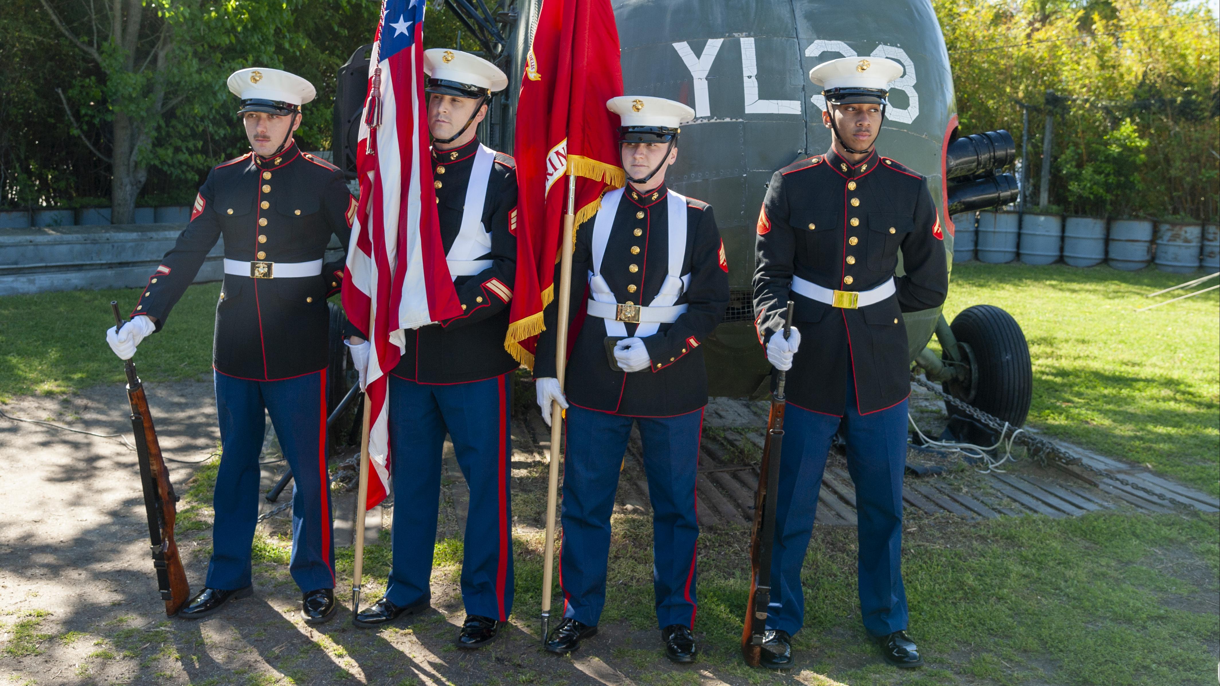 Honor guards salute in front of a Vietnam-era helicopter during a Vietnam Veterans Day event.