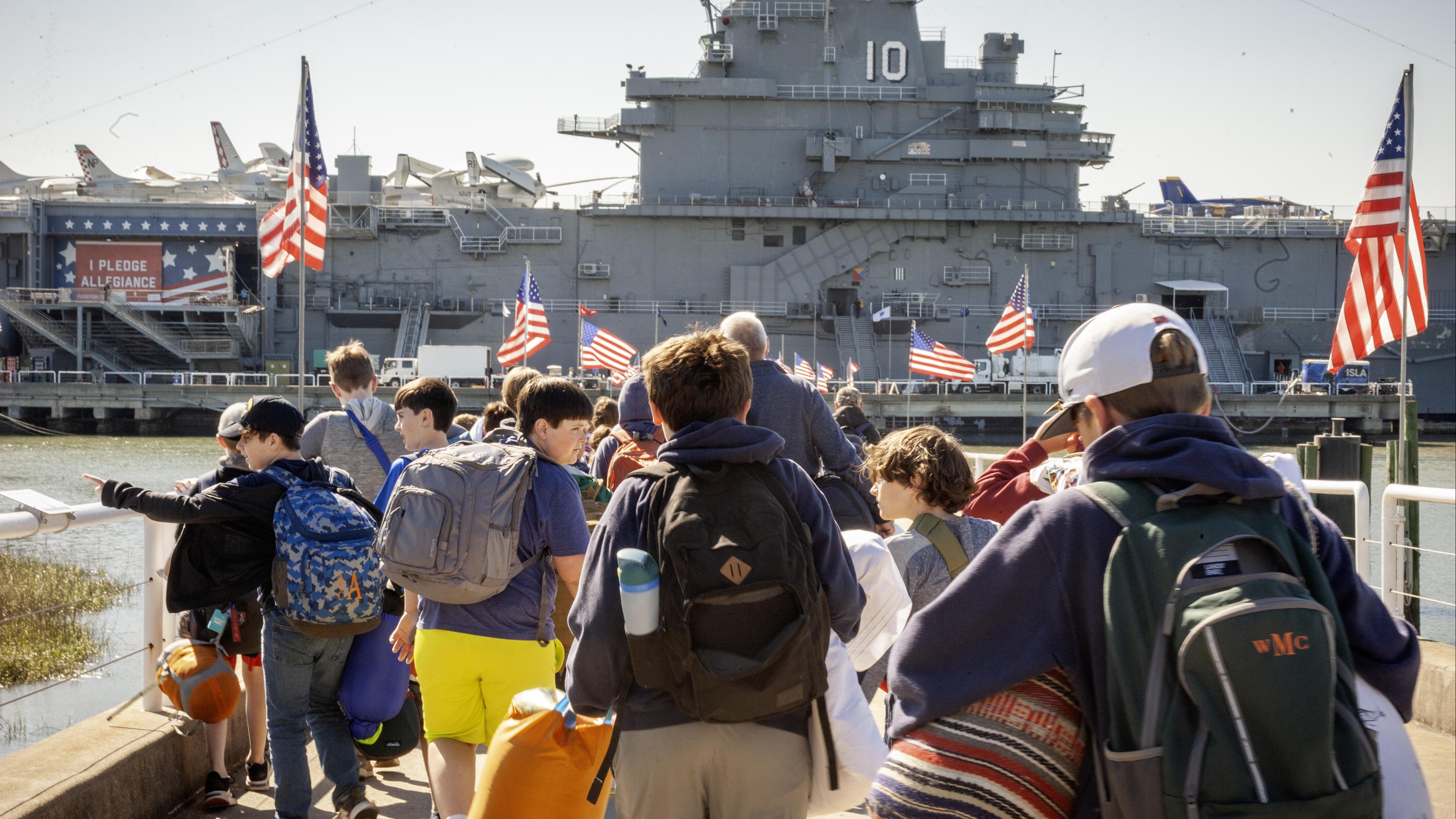 A group of campers walk to the USS Yorktown with their luggage.