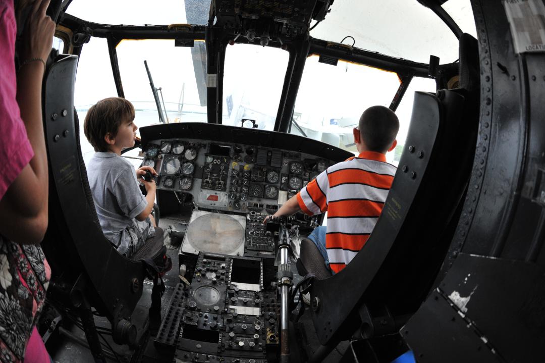 Two boys sit in the front of an aircraft by the controls