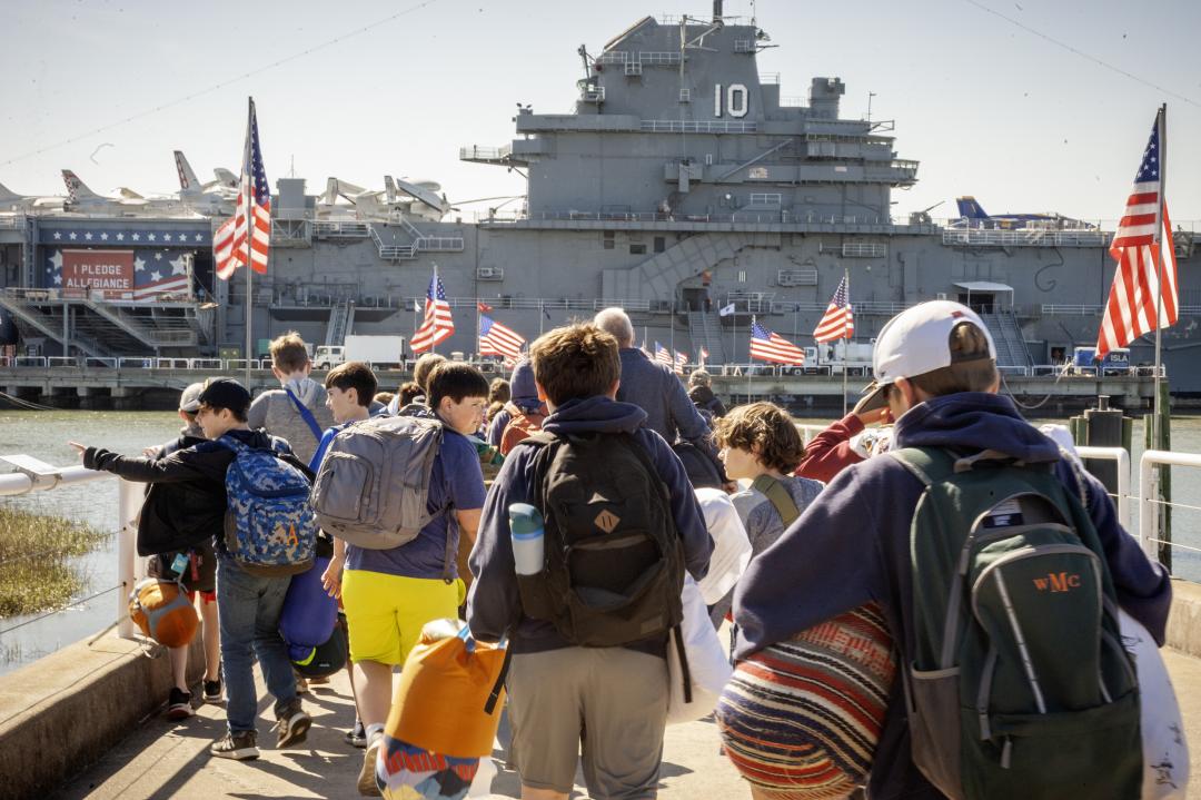 A group of campers walk to the USS Yorktown with their luggage.