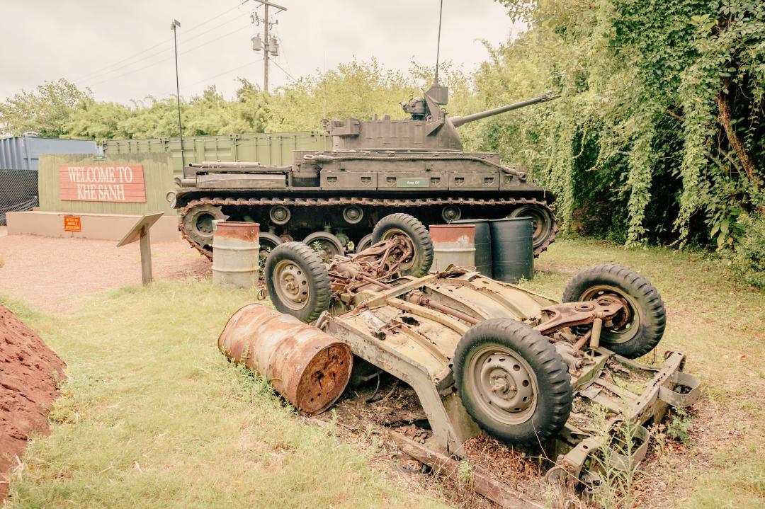 Large tank and overturned tank sit next to welcome sign for simulated "Khe Sahn" in Vietnam.