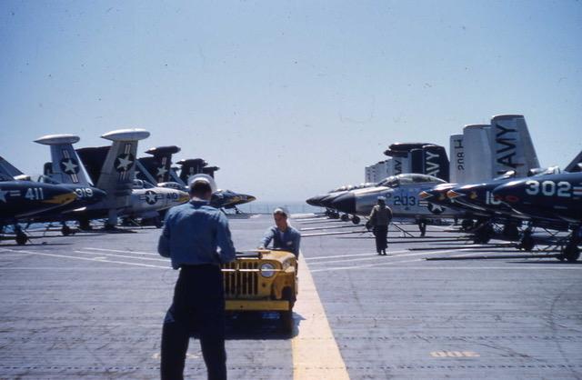 Sailors stand on the flight deck of the USS Yorktown surrounded by grey aircraft with American symbols.