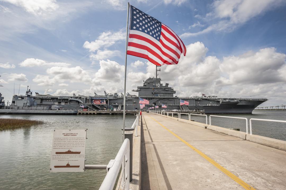 An American Flag waving in the foreground with the USS Yorktown behind.